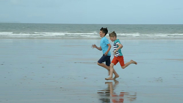 两个男孩在沙滩上玩慢镜头跑步比赛。视频素材