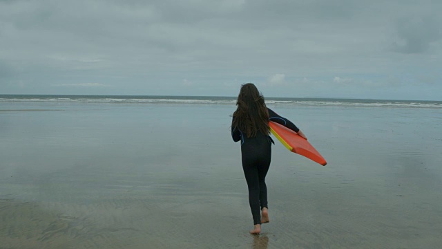 一个年轻的女孩跑到海洋与她的Bodyboard。视频素材