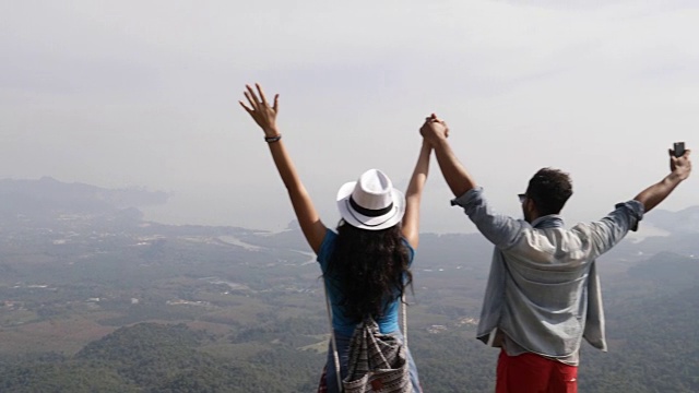 一对游客在山顶举起手享受自由男人和女人看风景的后视图视频素材