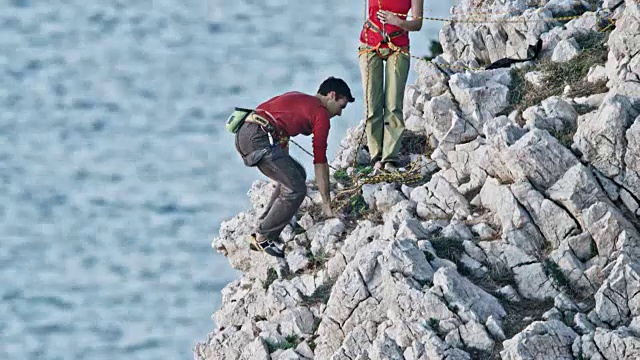 男性攀岩者到达崎岖的悬崖顶端，并与女性攀岩伙伴庆祝视频素材