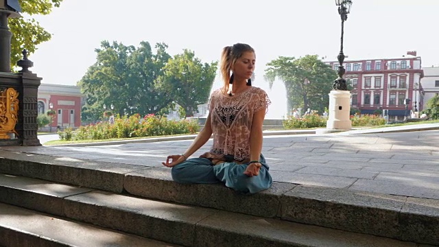一个女人在楼梯顶上莲花姿势冥想。年轻女孩在繁忙的城市背景下做瑜伽。慢动作视频下载