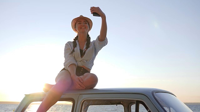 女孩对着海边的老爷车车顶自拍，女人对着老机器用手机拍照视频素材