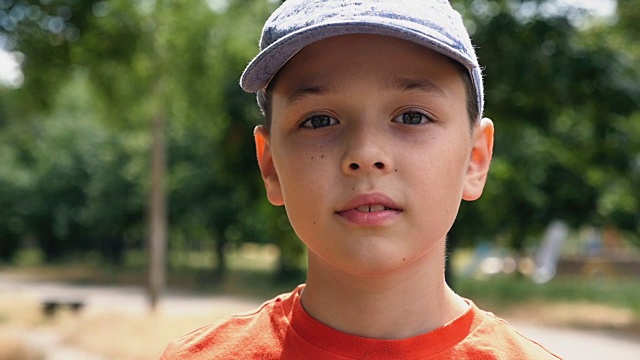 一个戴着帽子的聪明的男孩在慢动作站在公园里想着他的左边视频下载