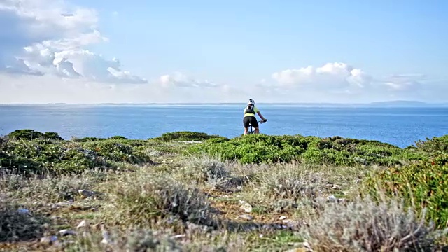 一个女人骑着自行车从山上下来，看到了美丽的海景视频下载