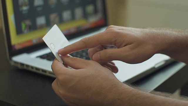 男人付账单，网上购物，插入信用卡号码。一名男子使用笔记本电脑和信用卡在网上购物。近距离视频下载