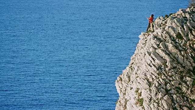 一名女性攀岩者到达了海面上锯齿状的悬崖顶端，她的男性伙伴向她表示祝贺视频素材