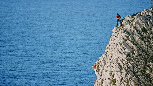 一名男性登山者在等待他的女性同伴爬上悬崖视频素材