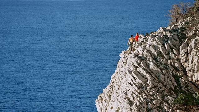 一名男性攀登者到达海面上的一个锯齿状悬崖顶端，并与他的女性攀登者交谈视频素材