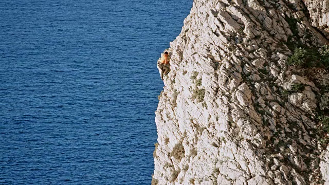 一名男子爬上悬崖顶端，他的女性伴侣在上面等着他视频素材