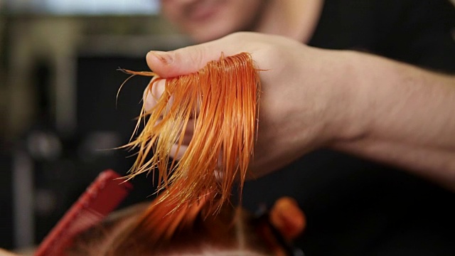 时髦的男理发师手里拿着一缕头发在美容院为一位女士理发。年轻女子在美发沙龙理发和打扮。在slowmotion拍摄视频下载