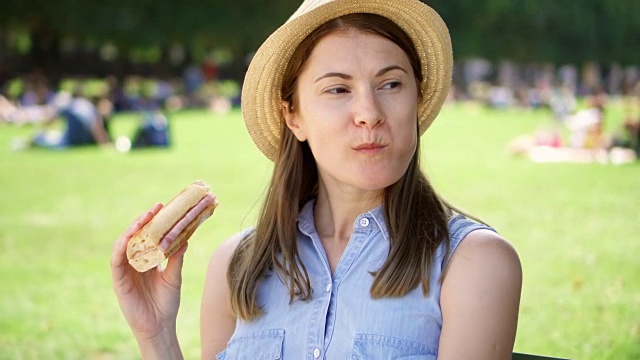 饥饿的女人在公园吃法棍面包。游客在公园享用午餐，享受夏日的阳光视频素材