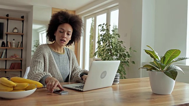 一位年轻的非裔美国妇女在笔记本电脑上输入电子邮件并接电话。视频素材