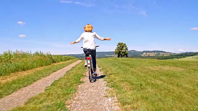 一个女人在一条土路上张开双臂骑着她的自行车视频素材