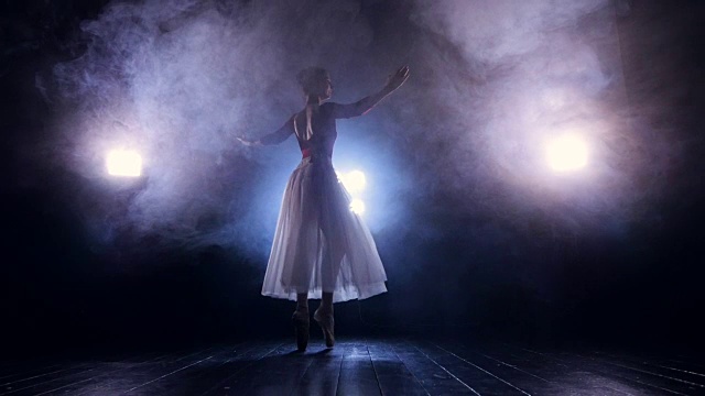 一位芭蕾舞演员在黑暗中慢慢转弯。视频素材
