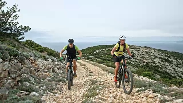 一对夫妇骑着他们的自行车爬上了一座小山，这是在海上的一条碎石路上视频素材