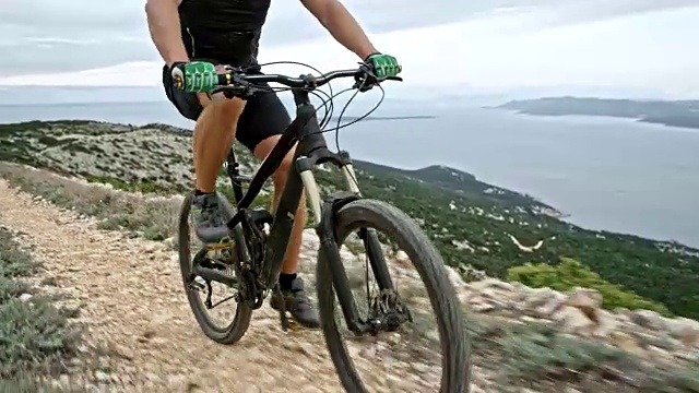 男性的腿推着自行车踏板，而骑在一个山脊上的海洋视频素材