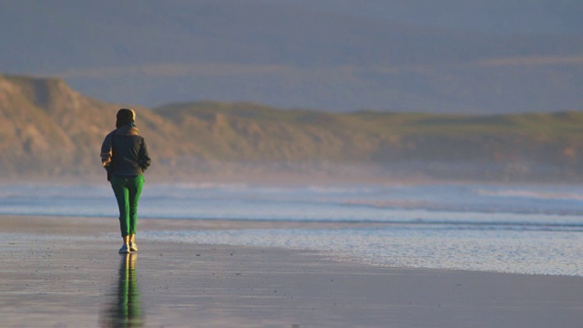 一名女子在潮湿的海滩上行走视频素材
