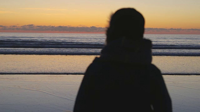 在日落时看海滩宁静的海浪的女人视频素材