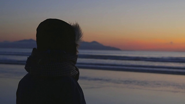 穿冬天衣服的女人在日落时看着海浪视频素材