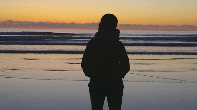 剪影女人看平静的海浪到达海岸在日落视频素材