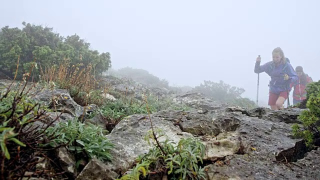 两名女性徒步者沿着一条多岩石的小道爬上雾蒙蒙的山视频素材