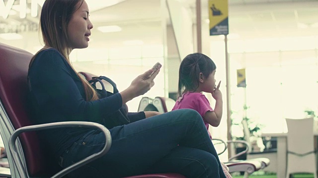 亚洲年轻的母亲和女儿在候机楼登机口用智能手机等待视频素材