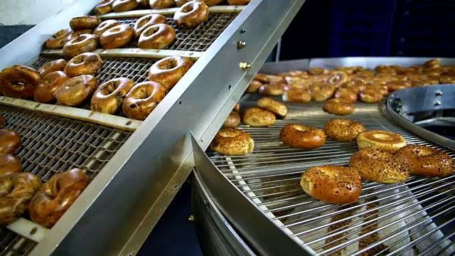 在面包房的工厂里，制作新鲜又热又美味的百吉饼——芝麻百吉饼正在传送带上进行运输和分类。视频素材