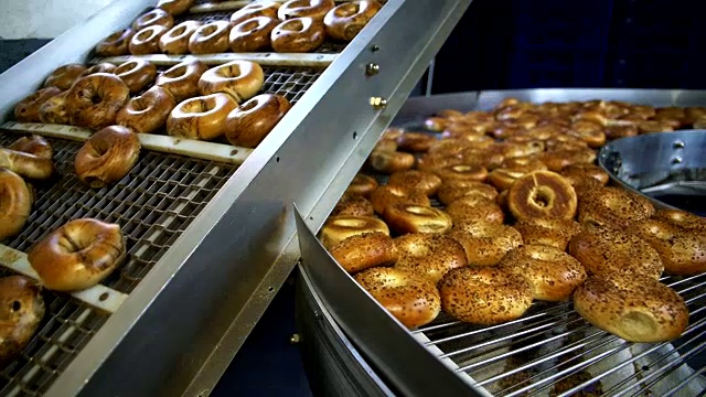 在面包房的工厂里，制作新鲜又热又美味的百吉饼——芝麻百吉饼正在传送带上进行运输和分类。视频素材