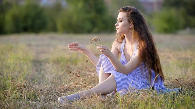 悲伤但非常美丽的女人平静地坐在田野里，手里拿着一些野花，思考着生命视频下载