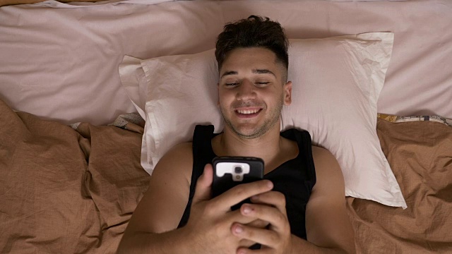一名年轻男子在睡觉前用智能手机在社交媒体上聊天视频素材