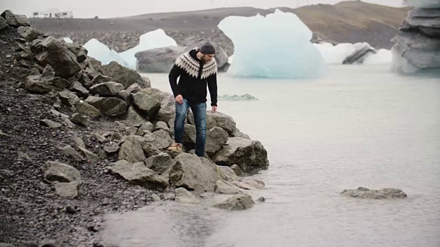 年轻英俊的男子站在Jokulsalon冰礁湖的岸边，看着冰岛的冰川视频素材