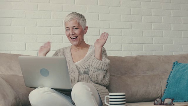 快乐成熟的女人发送亲吻和挥手，同时有视频聊天通过笔记本电脑。视频素材