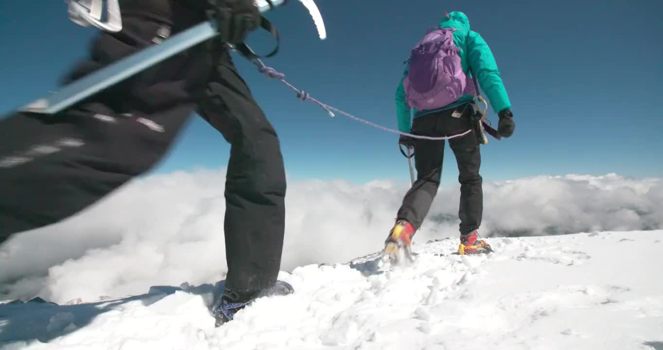 两名女性登山运动员在云层之上的高海拔处，在风吹过的冰川上穿越山脊。视频素材