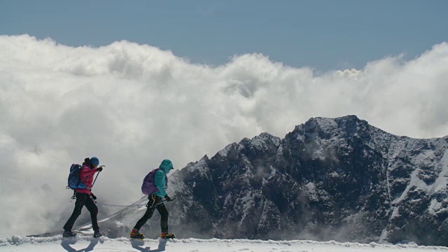 两名登山者正穿越冰川和山脊，远处乌云密布。视频素材
