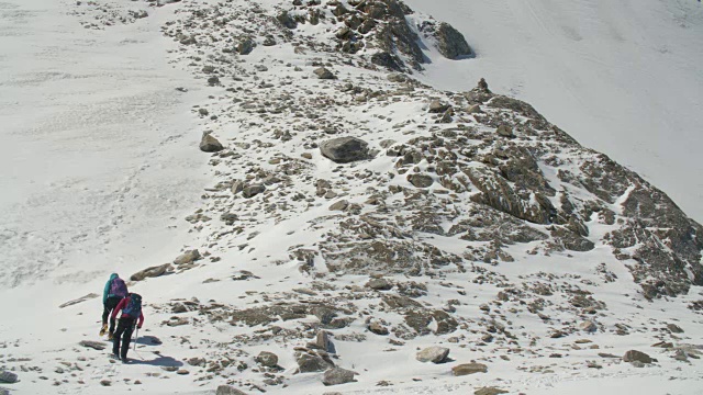 两名登山者正在岩石山脊上的冰川边缘攀登。视频素材
