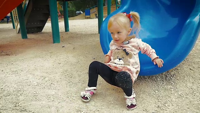 慢镜头:一个三岁的小女孩从操场上的滑梯上下来。视频素材
