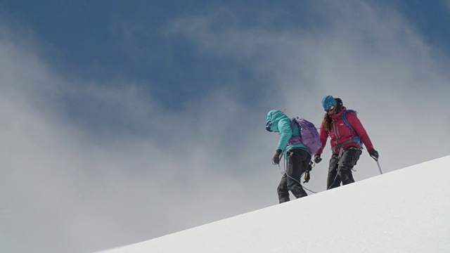两名被绳子系在一起的女性登山者在云层翻滚时一起穿越冰川。视频素材