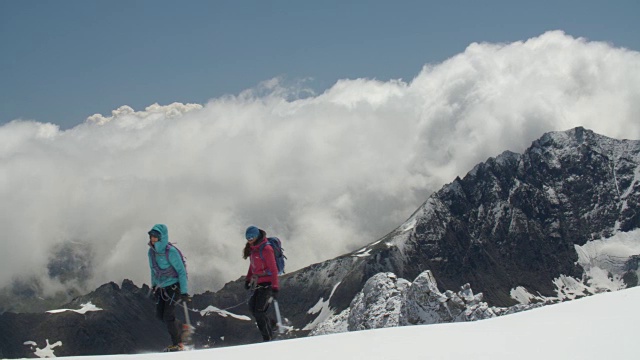 两名女登山运动员穿过高山中的冰川山脊，风暴云正在酝酿。视频素材