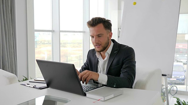 成功的商人在会议室用笔记本电脑上网工作，在智能手机上愉快地交谈视频下载