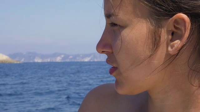 年轻女子坐在小船上凝视着大海，背景是一座小岛视频素材