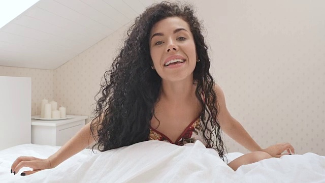 可爱的黑发女子在床上为相机摆姿势视频素材