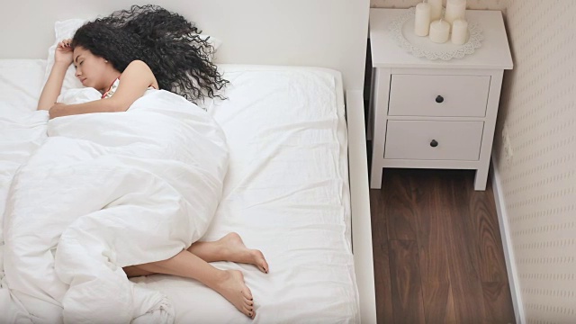 漂亮的黑发女孩睡在白色的床上视频素材