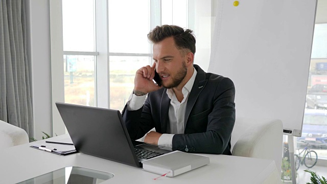 在现代办公室里年轻老板的电话交谈，成功的商人在网上用笔记本电脑工作视频下载