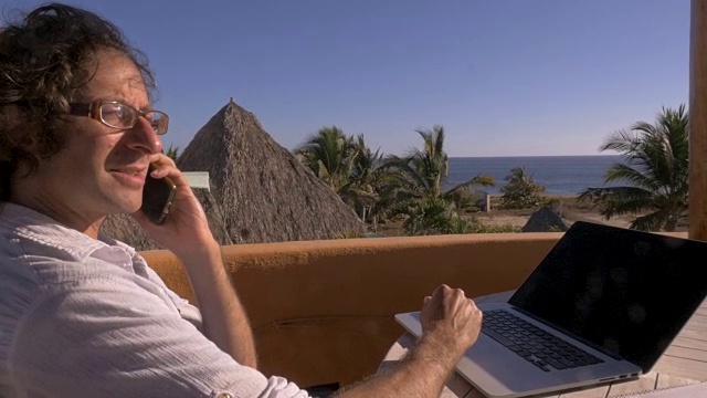 一名男子一边在海滩的家庭办公室里工作，一边用智能手机聊天视频素材
