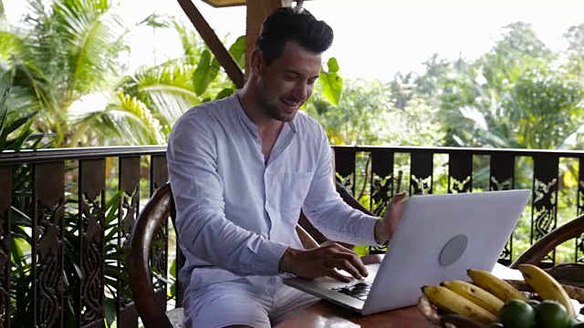 快乐微笑的男人在阳台上使用笔记本电脑，休闲商人在户外用电脑打字视频素材