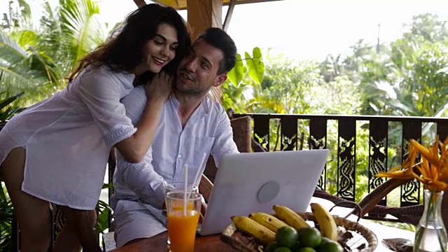 年轻夫妇一起使用笔记本电脑在夏季森林的露台上，美丽的男人和女人上网聊天视频素材