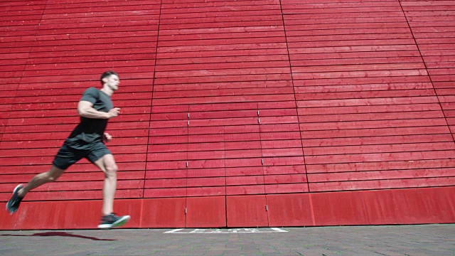 一个年轻人跑过一堵红墙的慢镜头。视频素材