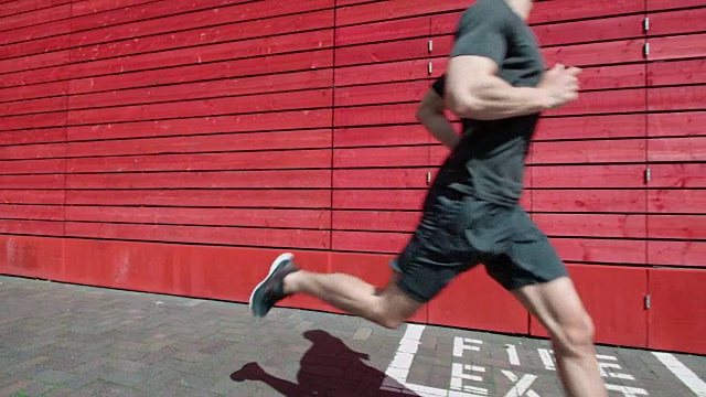 一个年轻人跑过一堵红墙的慢镜头。视频素材