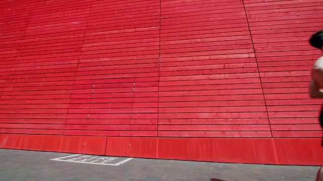 一个肌肉发达的年轻人在慢镜头中跑过一堵红色的墙。视频下载