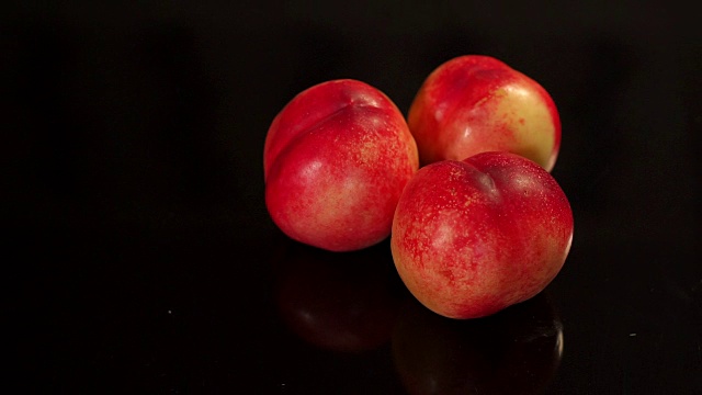 三个成熟的桃子在黑色的背景下。视频下载